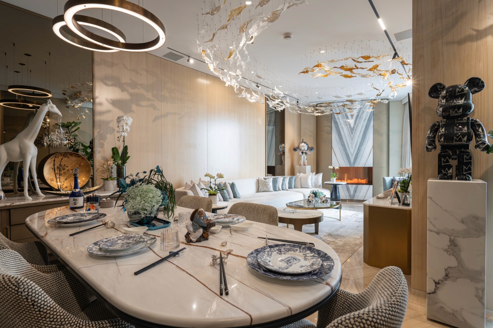 Luxuriously designed modern living room in Five Dubai with a marble dining table set for four, featuring contemporary decor, a giraffe sculpture, a geometric fireplace, and artistic ceiling installations.