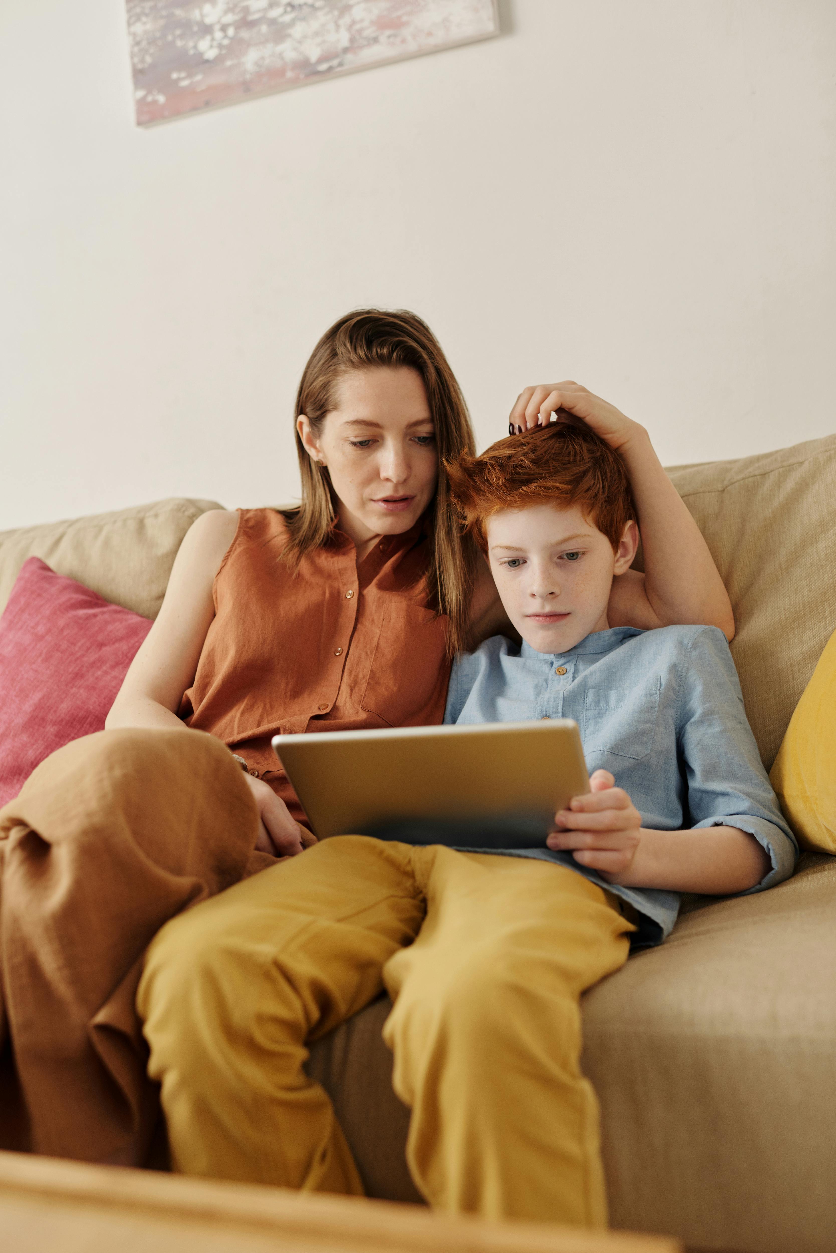 A mother and her son are sitting together, using a tablet to work on homework