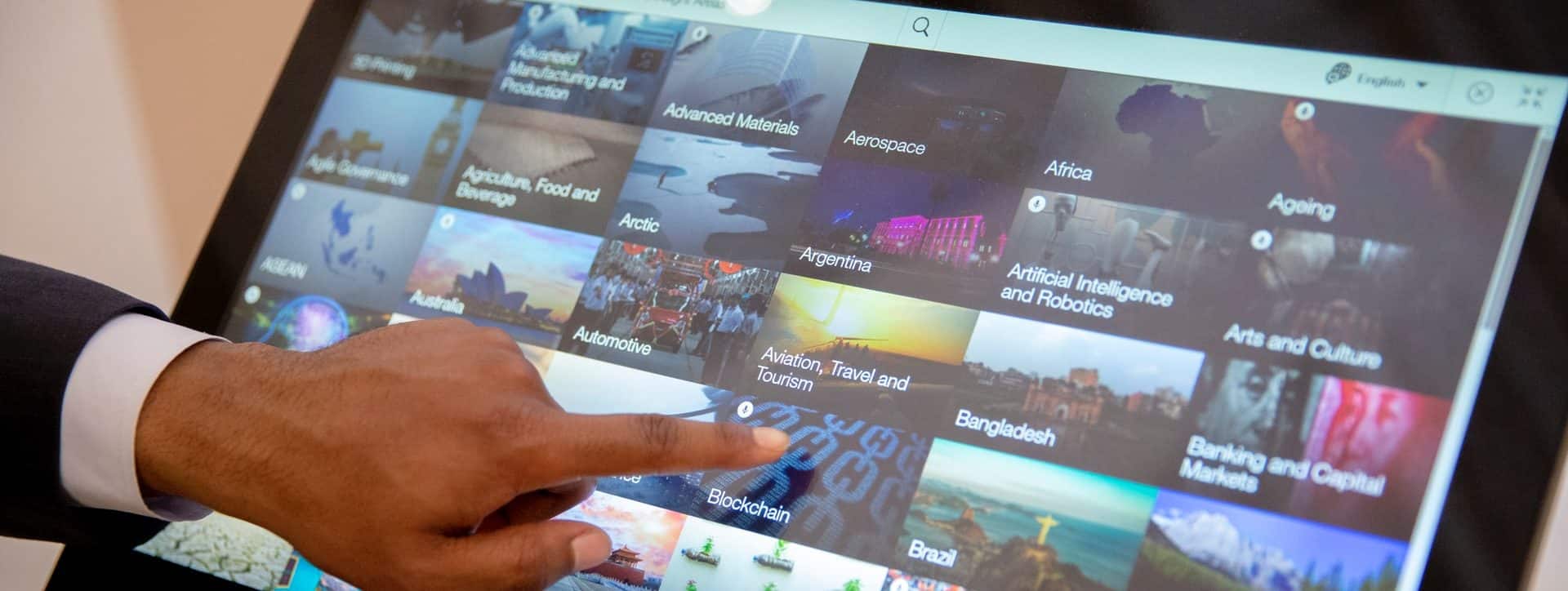 Person interacting with digital touchscreen displaying global topics like aerospace, automotive, and artificial intelligence.