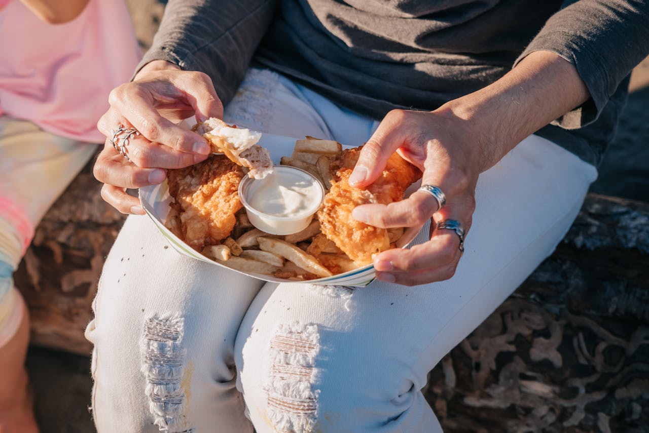 A close up of a young woman eating fish and chips.