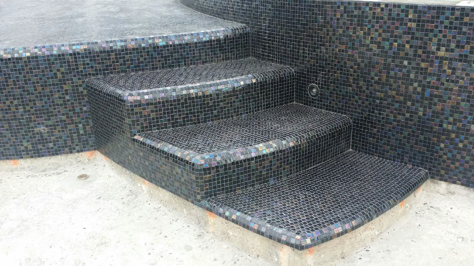 Pool steps in close-up — individual tesserae of the near-black blend, with the iridescence visible.