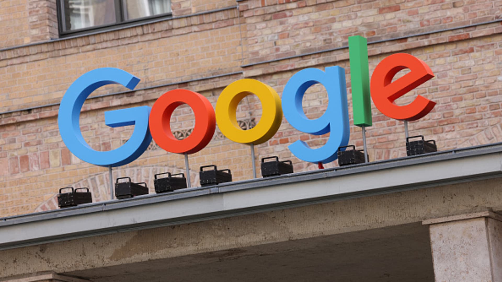 Large Google logo in bright blue, red, yellow, and green letters mounted on the rooftop of a brick building, against a light background.