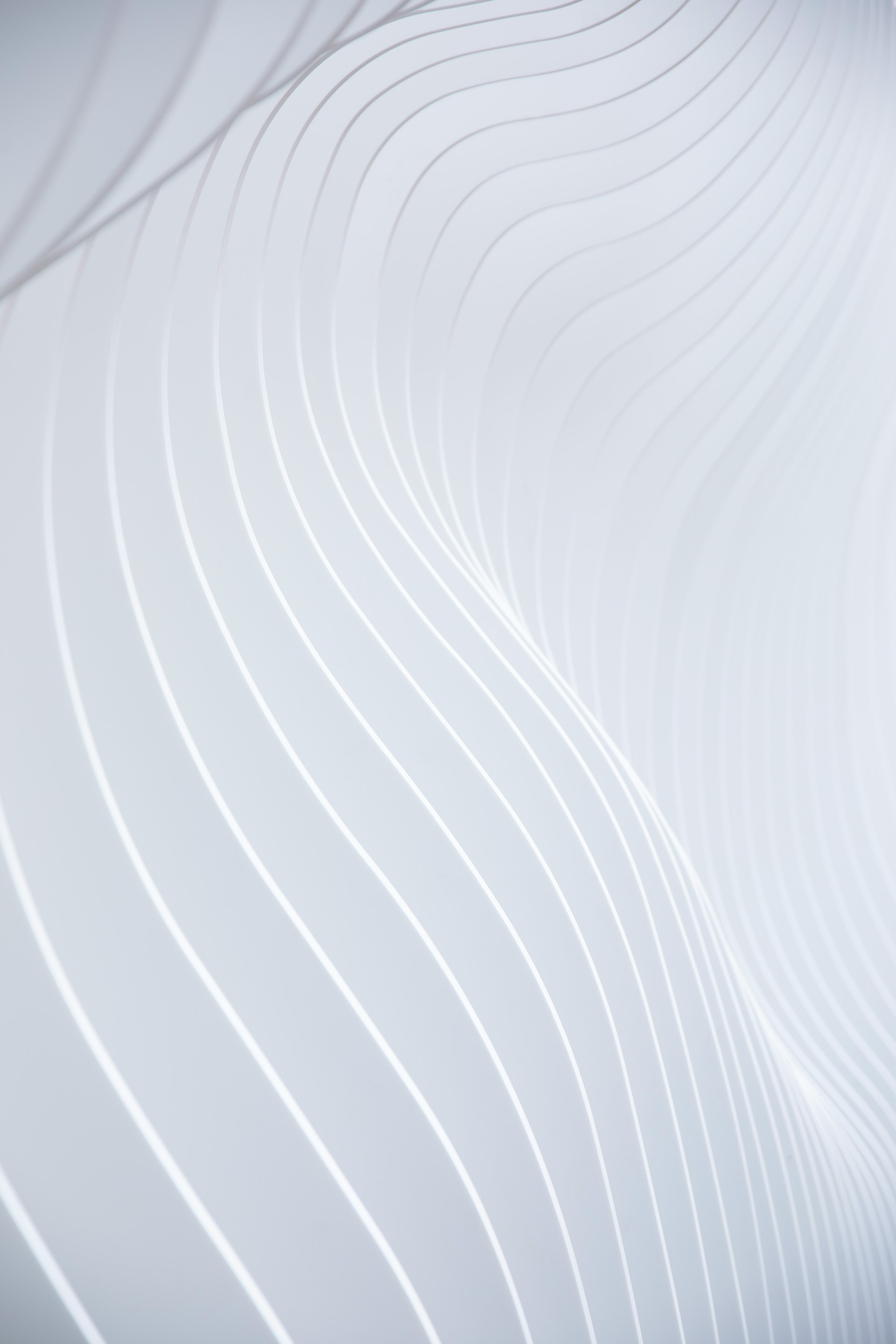 Abstract white surface with smooth, wavy lines creating a flowing, three-dimensional pattern.
