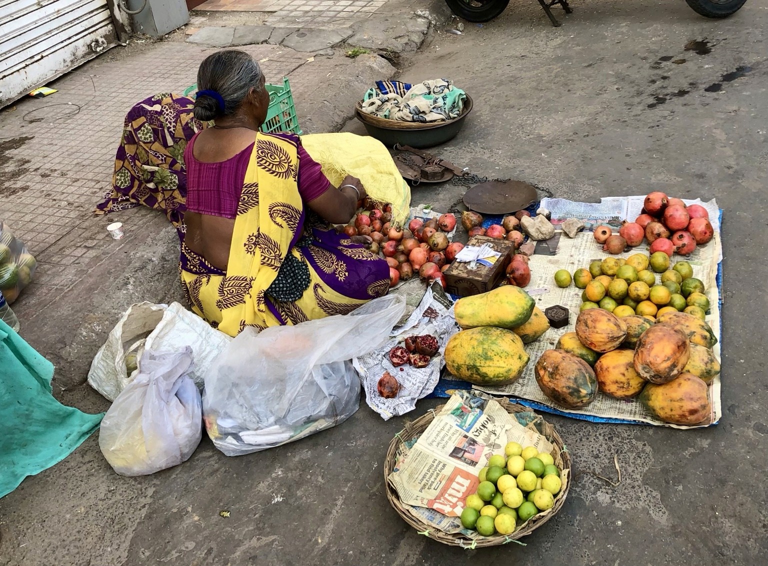 A fruit vendor in a yellow and purple sari surrounded by papayas and other produce. Photograph by Pranjali Shah.