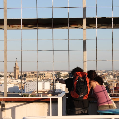 兩個人倚著欄杆，透過金屬格子俯瞰城市景觀，可以看到建築物和遠處的塔樓。