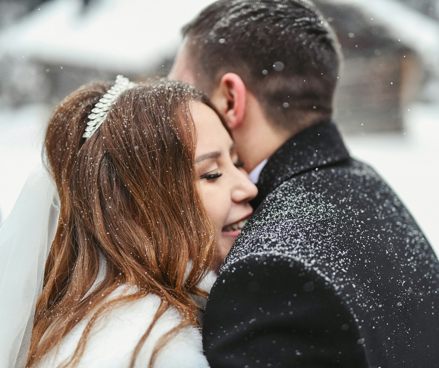 The groom holding the bride close as snow falls on them