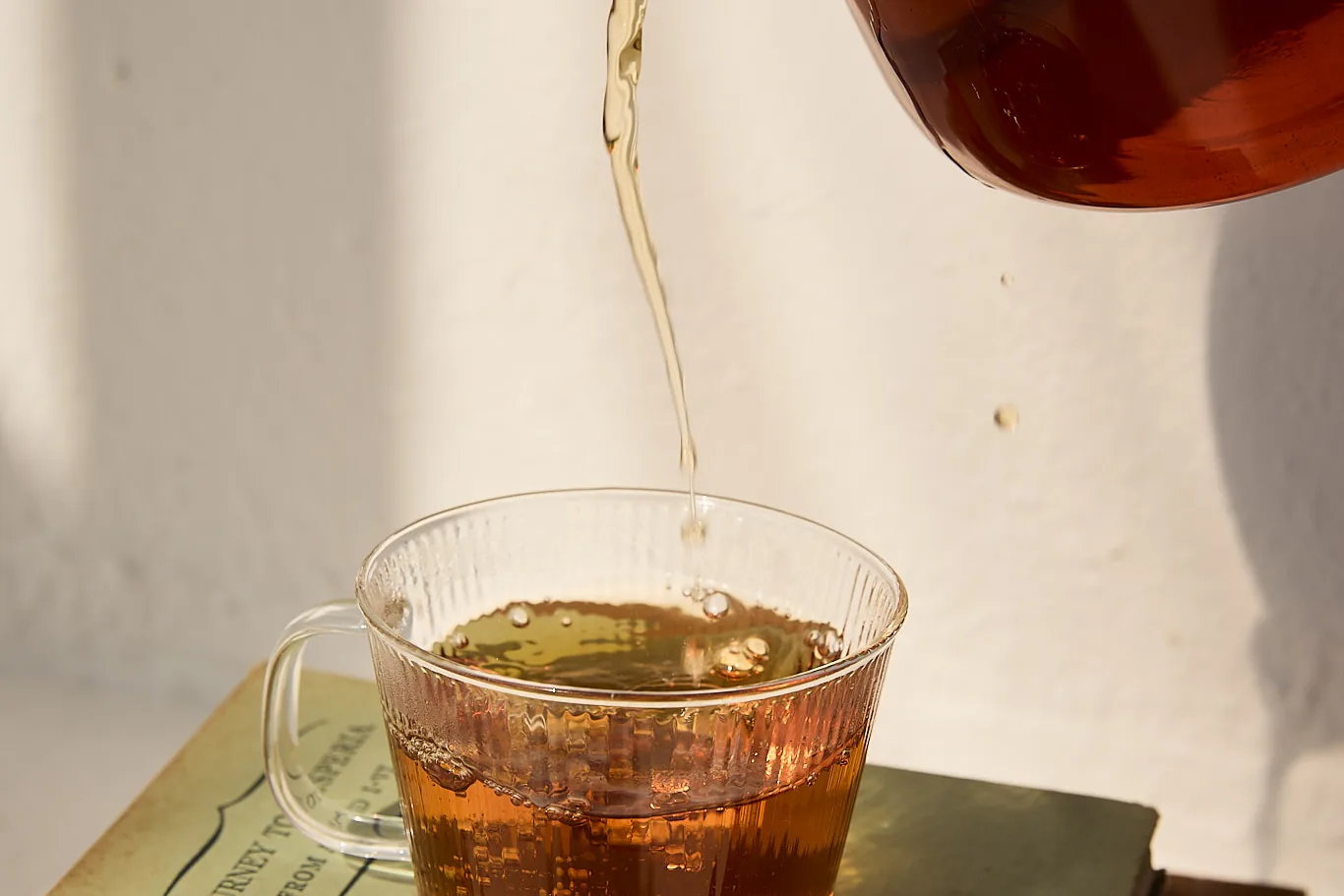 Sēkret tea poured from a glass teapot into a cup resting on a stack of books