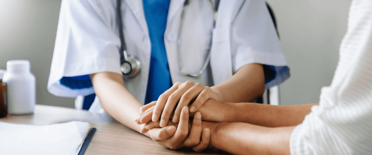 A doctor holding a patient's hand, symbolizing trust and empathy, for a blog post on patient testimonial videos for healthcare brands.