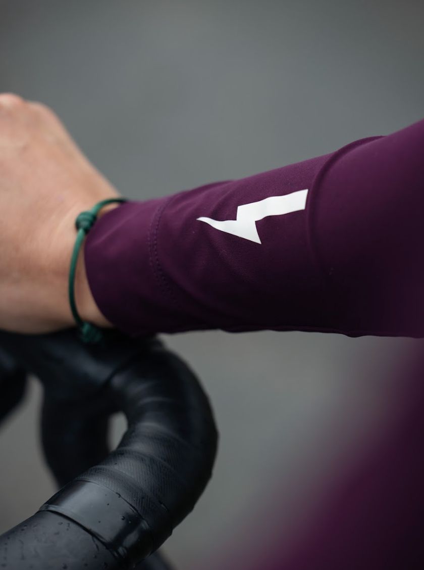 Close-up-of-a-hand-resting-on-black-bicycle-handlebars-showing- the-sleeve-of-a-burgundy-cycling- jersey-with-a-white-lightning-bolt- graphic