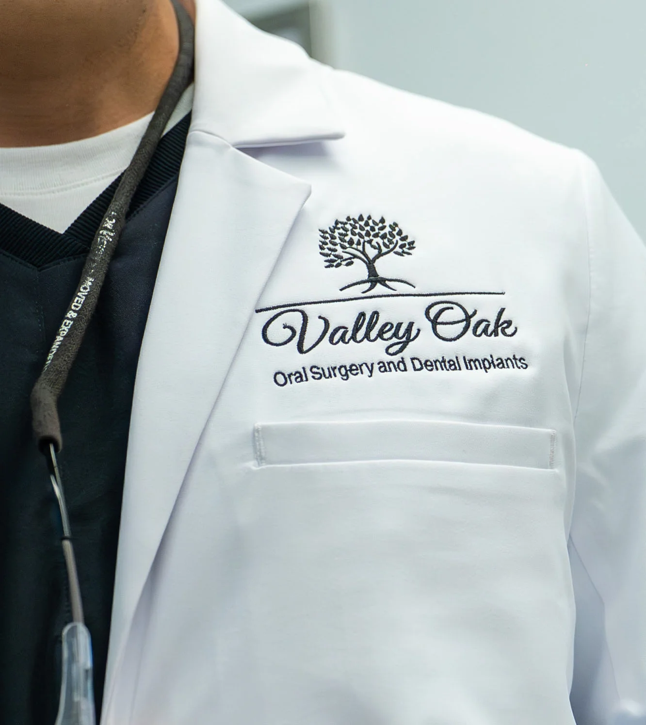 Close-up of a Valley Oak Oral Surgery medical coat featuring the practice logo embroidered on a white doctor’s coat in a modern clinical setting.