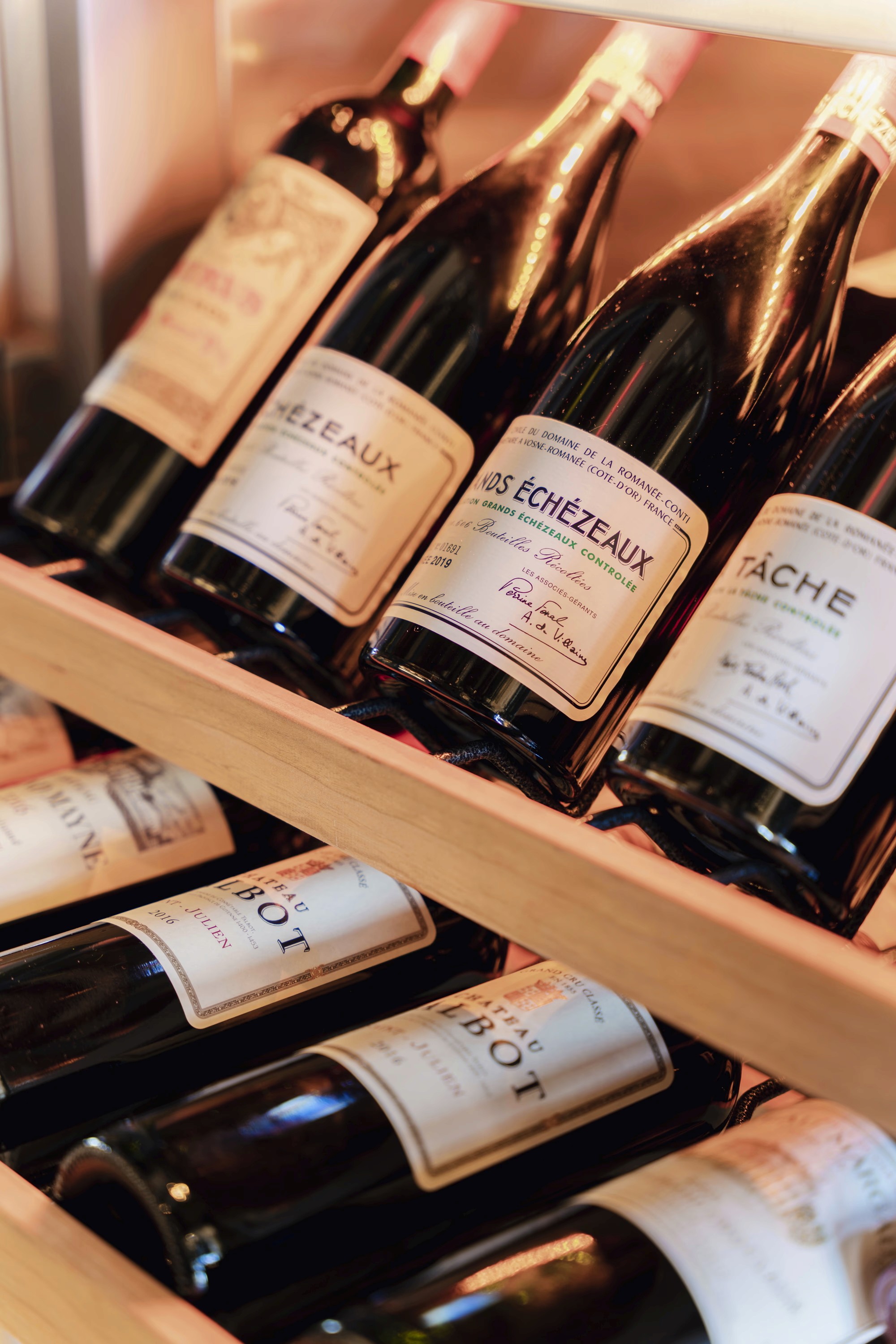A wooden wine rack displaying several bottles of wine with labels facing forward.