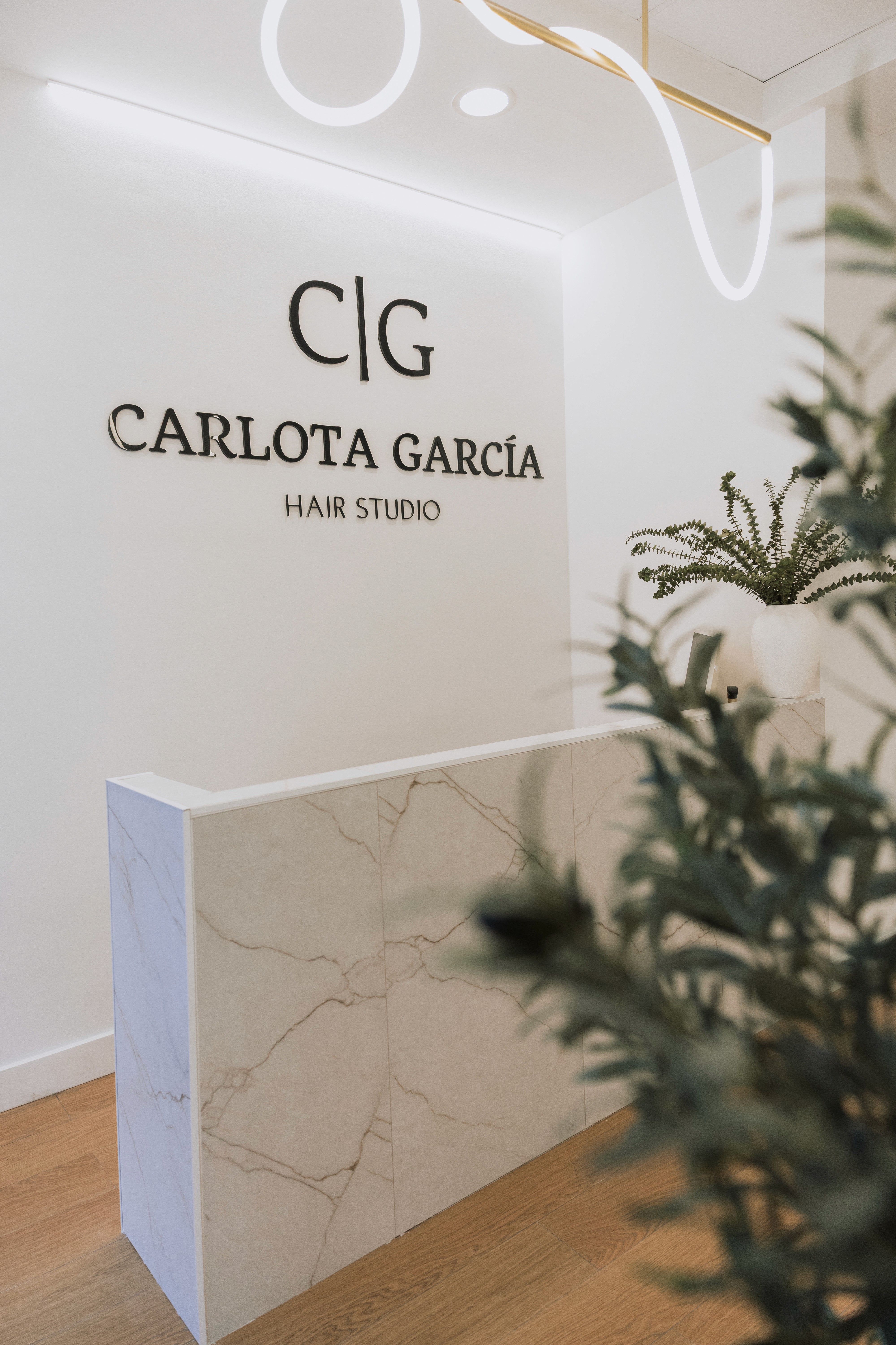 A serene and elegant spa space with wooden reclining chairs and white cushions. Golden sunlight filters through a cascading water feature, creating a peaceful atmosphere. Tropical plants and candles add to the relaxing ambiance.