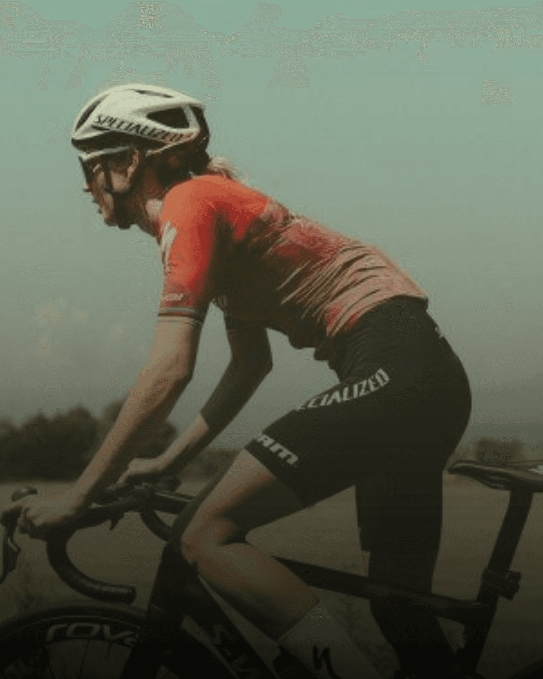 A smiling woman with curly hair is posing in a warmly lit indoor setting. She wears a dark-colored shirt.