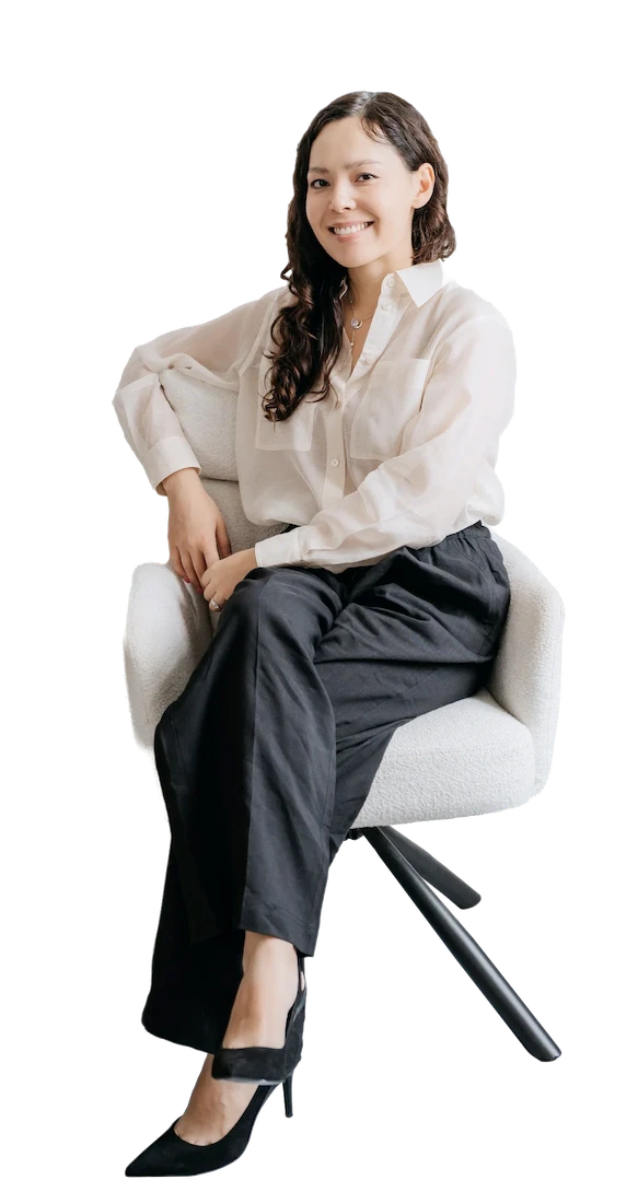 Kristina Lo sitting cross-legged on a white chair and smiling, looking warm and welcoming.
