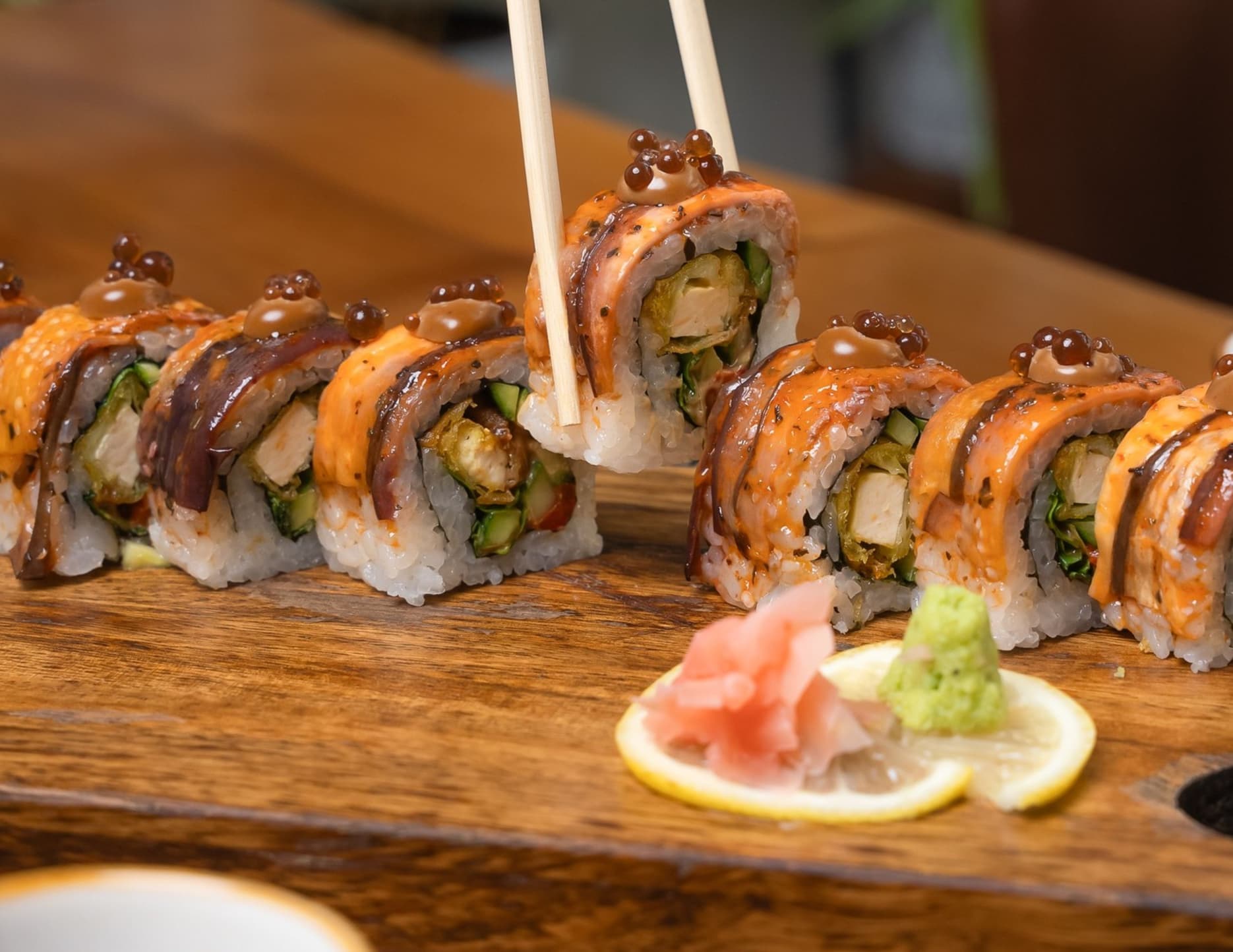 A vegan food with a sushi topped with glazed eggplant, tofu tempura, vegetables, and black garlic mayo dip to complete the dish.