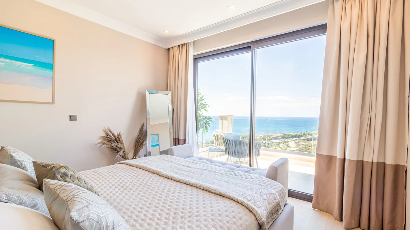 White Cedar House Mediterranean bedroom with soft neutral bedding and sliding doors to a sea-view terrace