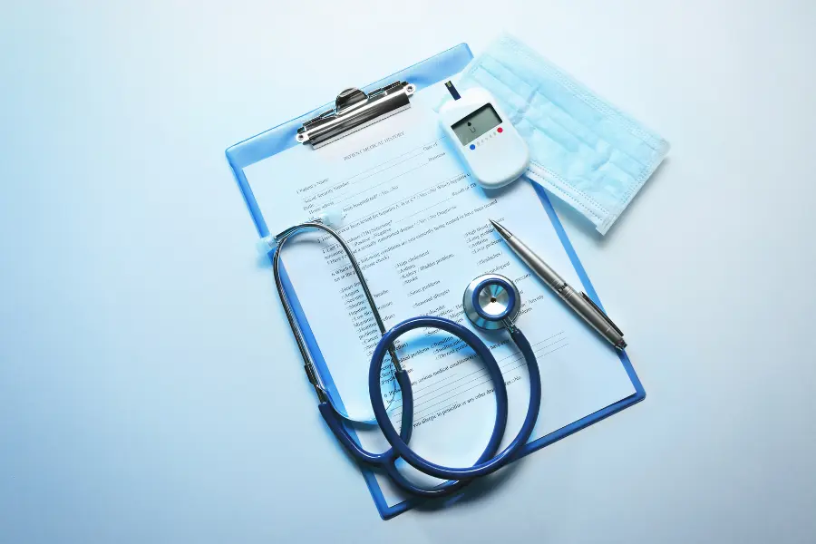AI medical coder organizing patient records shown by a clipboard with a stethoscope, glucose monitor, pen, and face mask on a blue surface.
