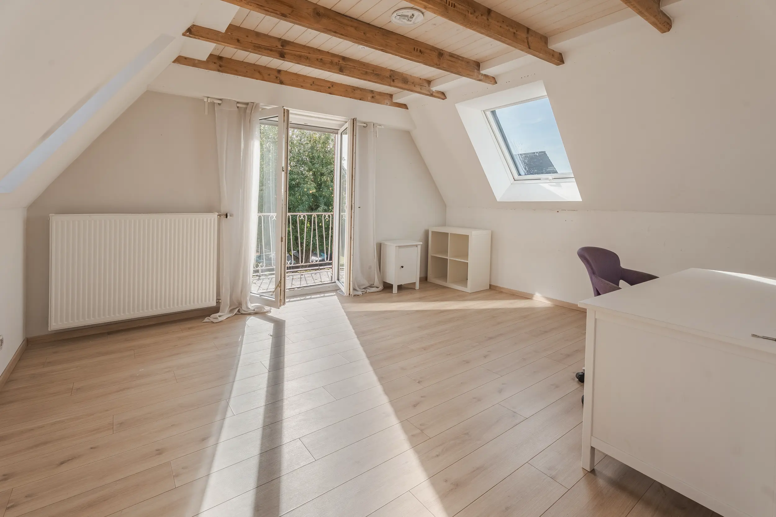 Dachzimmer im Einfamilienhaus in Südlohn-Oeding mit sichtbaren Holzbalken, Schreibtisch und offener Tür zum Balkon.