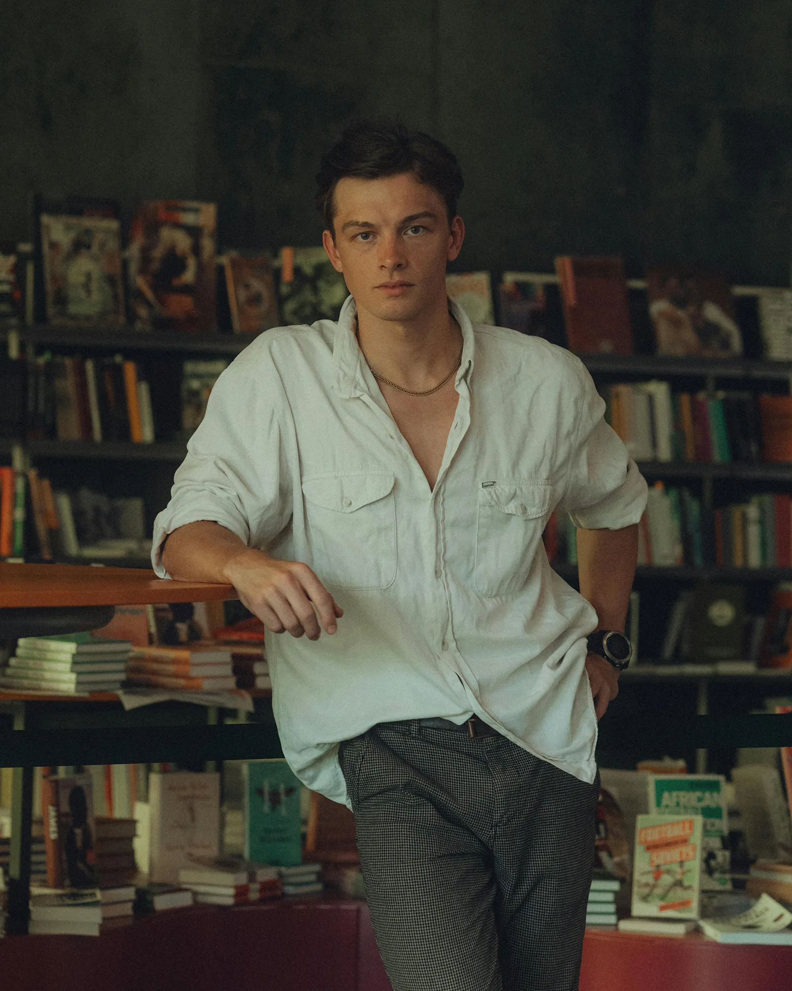 A young man leaning on a stack of books in a library