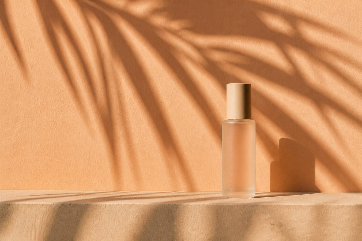 Palm-frond shadows across a pale peach stucco wall with an unbranded bottle on a concrete ledge
