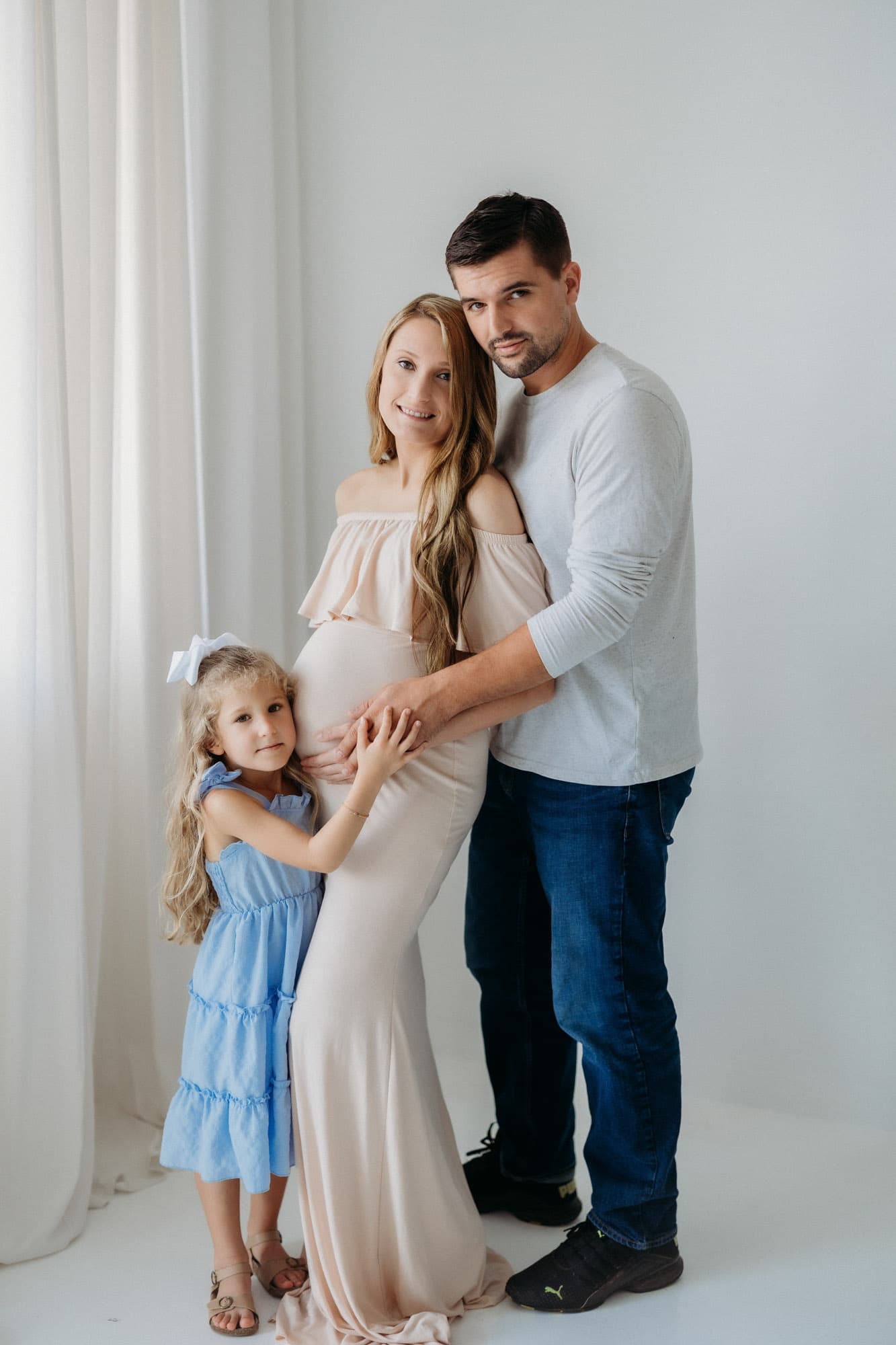 A family poses together in a natural light studio, highlighting the mother’s pregnancy at Revelator Studio in Shreveport, perfect for maternity photography.