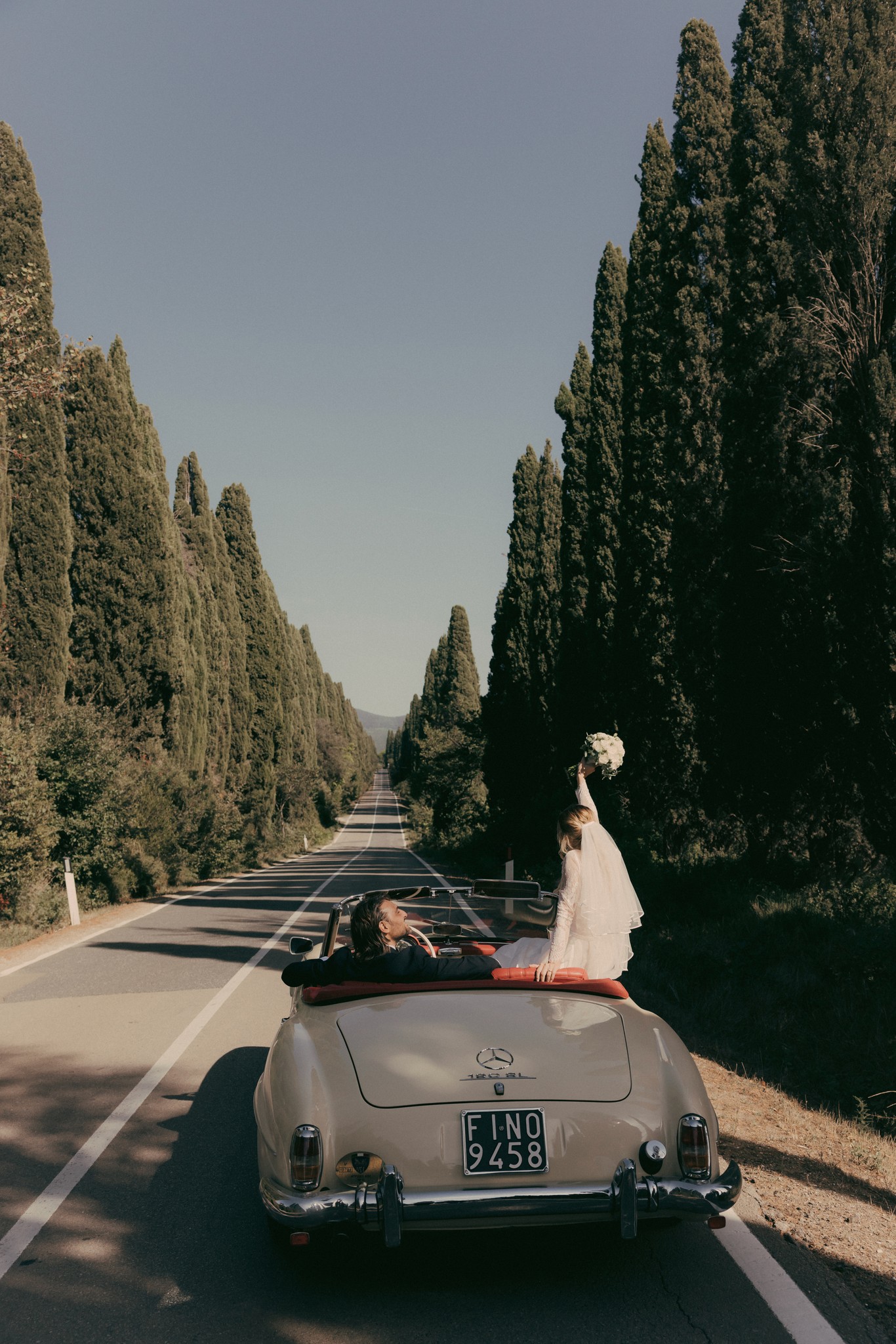 Sposi in fuga su Mercedes d'epoca nel Viale dei Cipressi di Bolgheri, circondati da riso e luce naturale