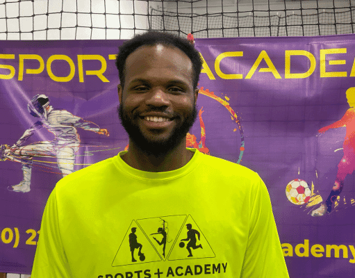 SportPlus Head Basketball Coach A-Montre posing for a headshot wearing a SportPlus neon shirt in front of a SportPlus Academy sign in our gym