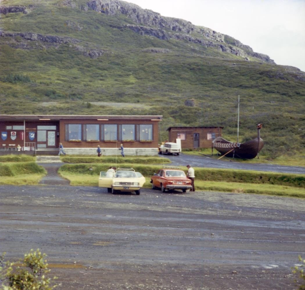 Cars parked outside Hótel Flókalundur, with a Viking ship replica beside the building