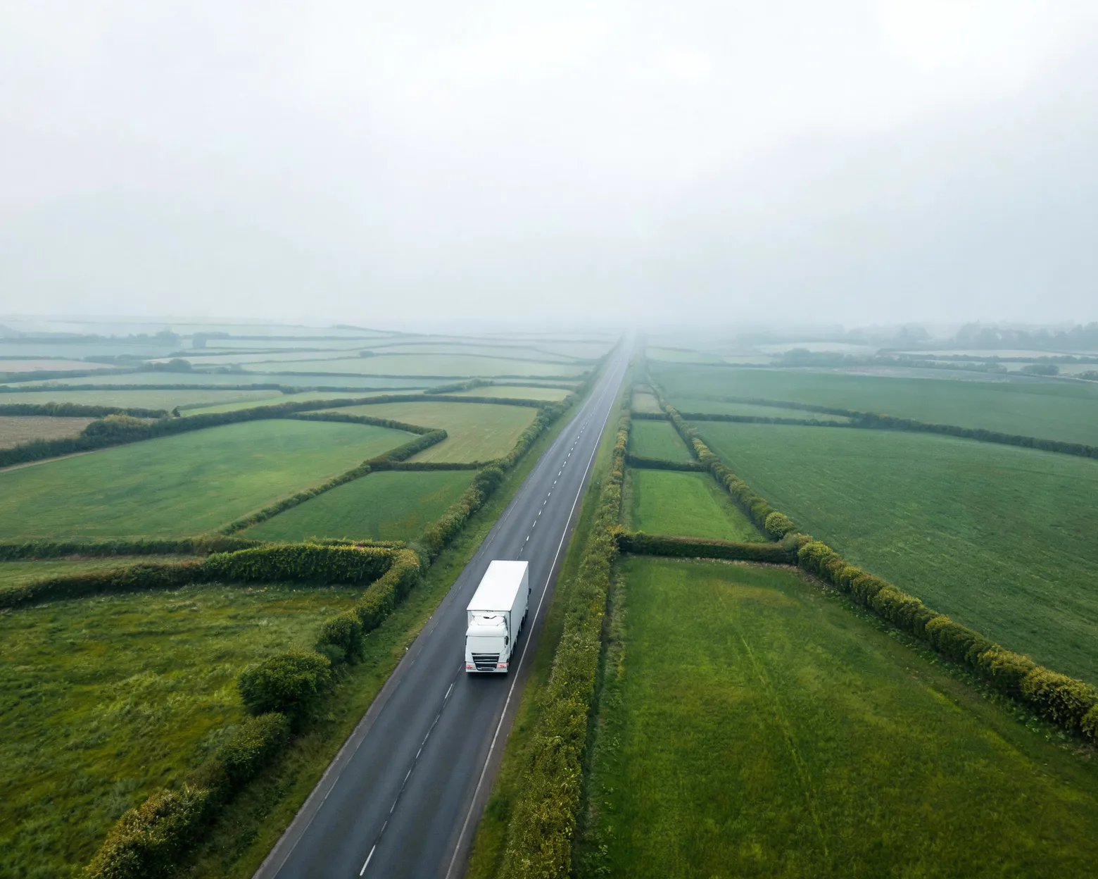 Aerial view of a white refrigerated truck on a long country road through green farmland