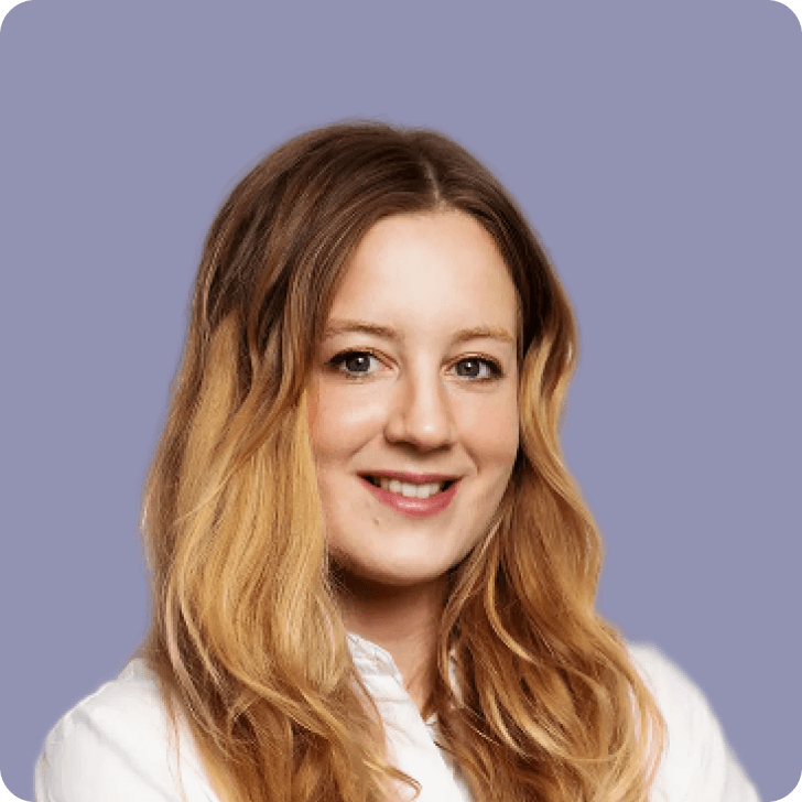 A smiling blonde woman in a white shirt in front of a purple background