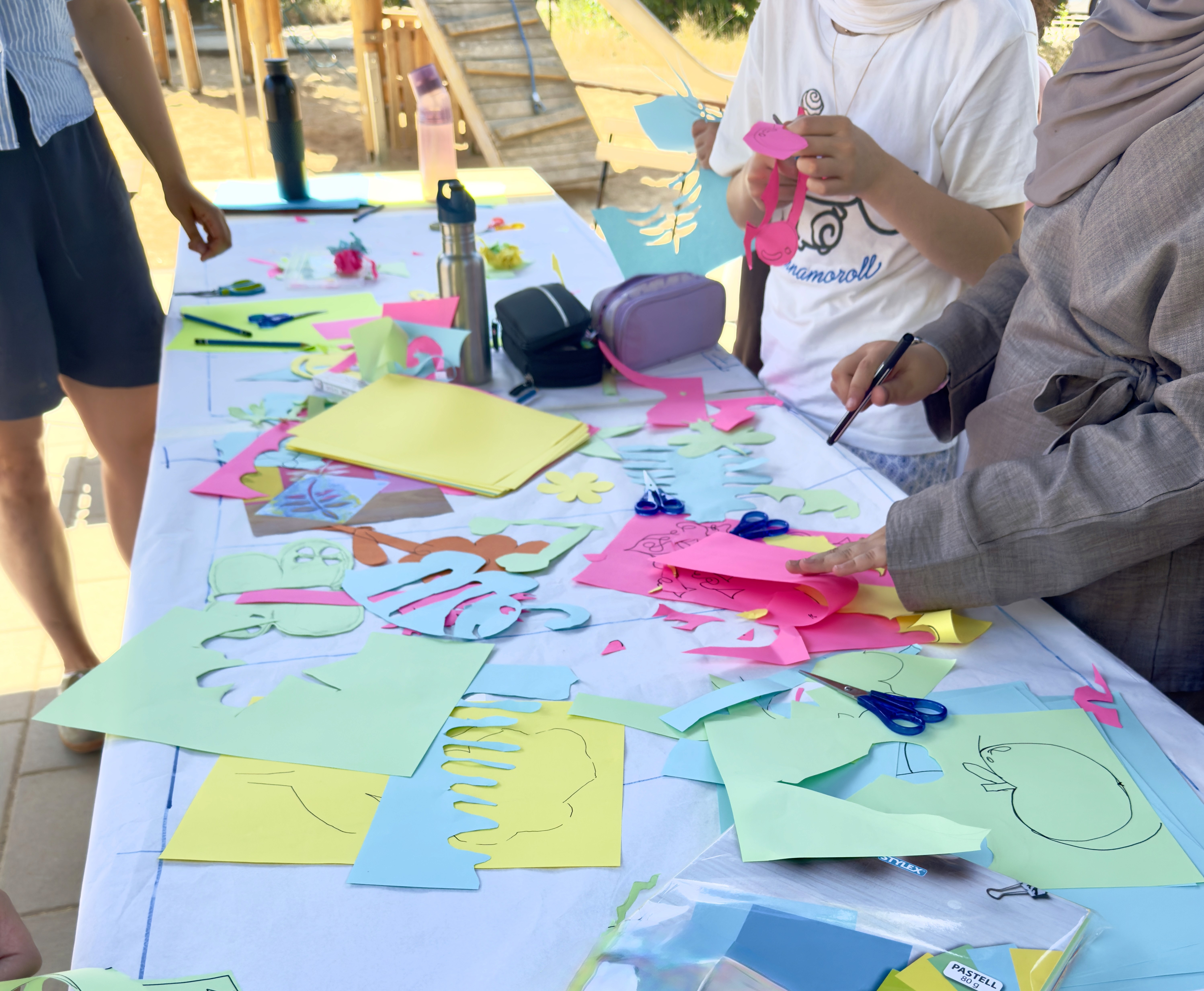 Partizipative Workshop-Präsentation im Freien am Genovevahof: Eine Moderatorin zeigt einer sitzenden Gruppe ein handgezeichnetes Quartiersbild, im Hintergrund graffitibemalte Hauswände bei Sonnenschein.