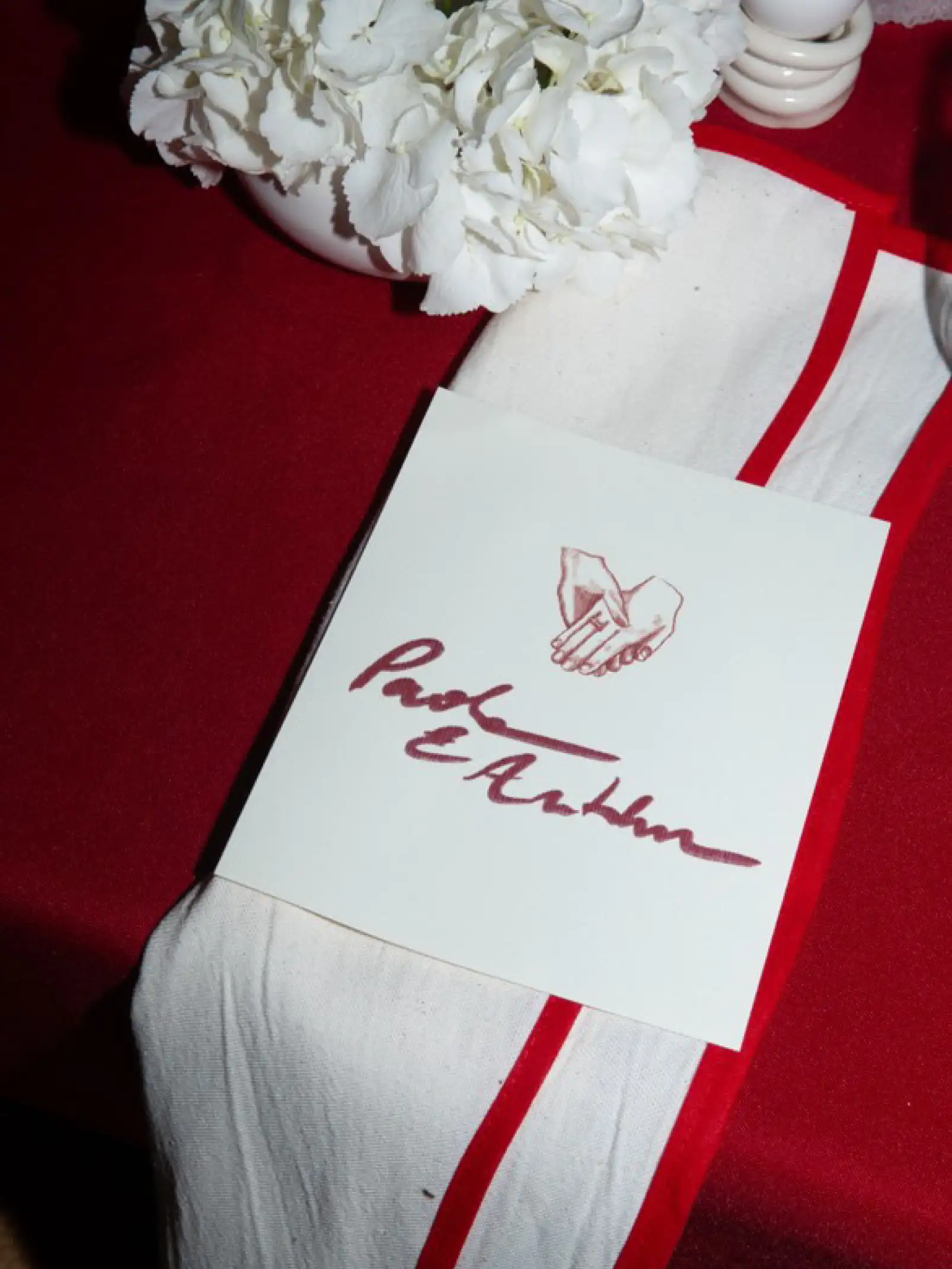 Detalle de papelería de boda sobre mantel rojo con flores blancas para marcas de eventos que valoran identidad visual, coherencia y diseño artesanal.