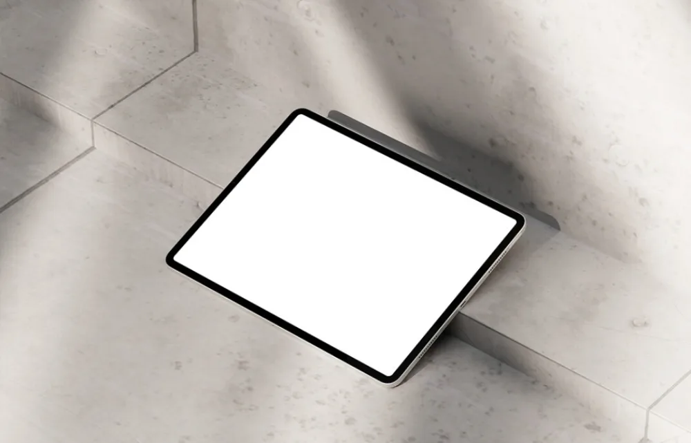 iPad mockup with a blank white screen, placed on a concrete staircase. The setting is illuminated by natural light, casting soft shadows across the textured surface for a modern aesthetic.