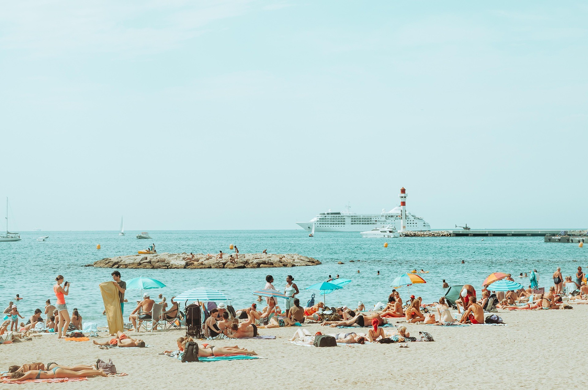 Plage de Cannes avec touristes, mer turquoise et phare du port.
