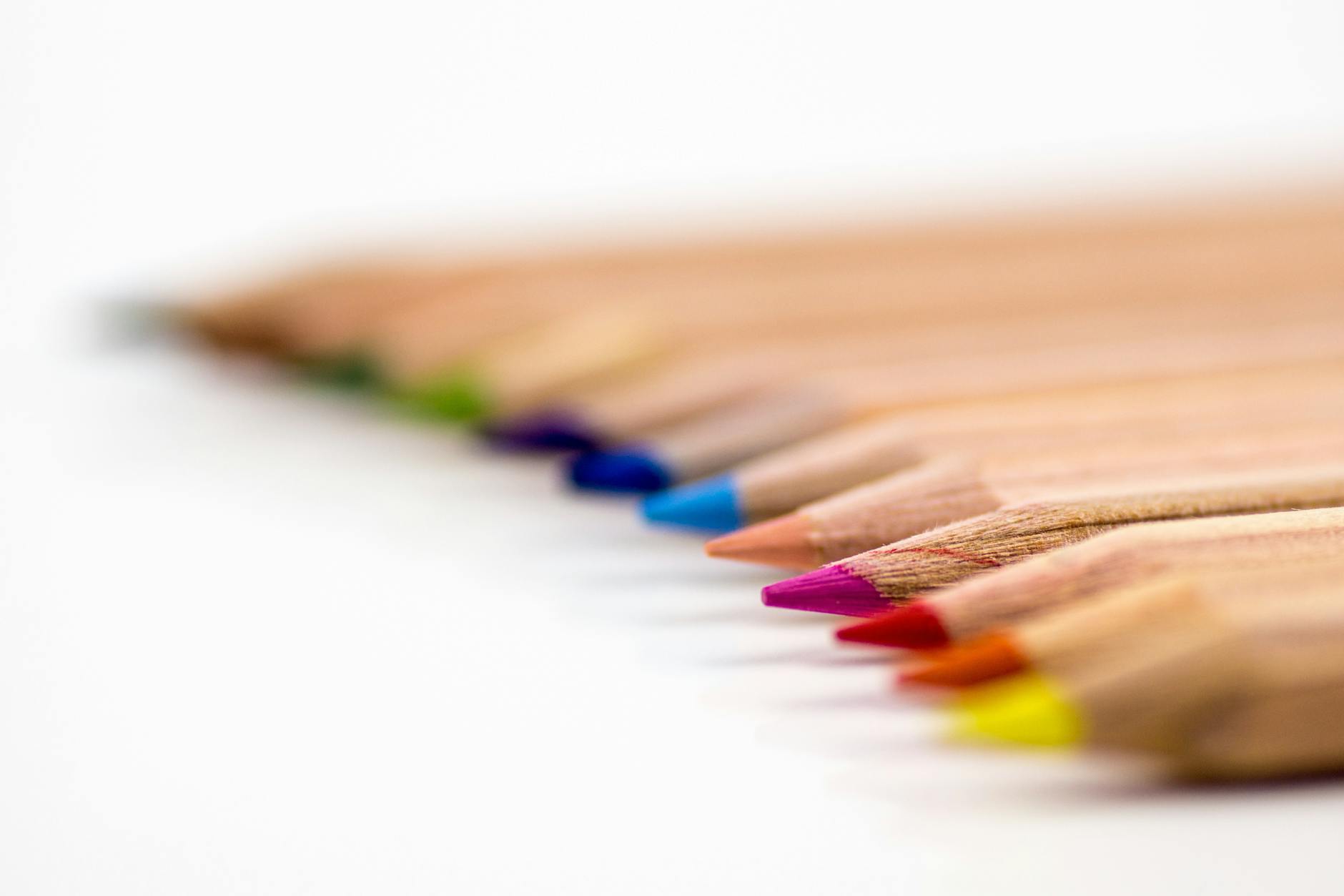 Close-up of colorful pencils aligned on a white surface, showcasing vibrant creativity.