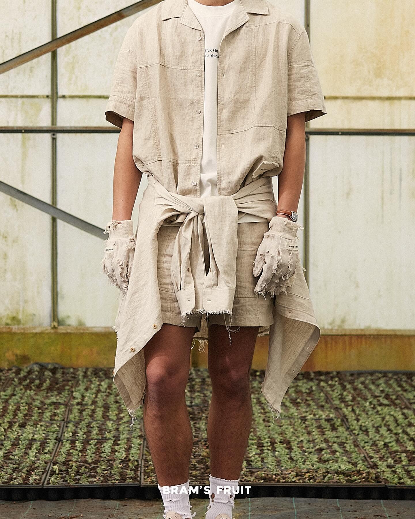 Détail dans une serre sur une tenue beige inspirée du jardinage avec surchemise, blouson noué autour de la taille et short en toile épaisse