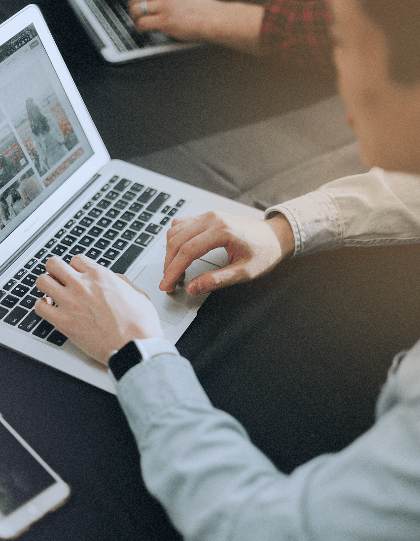 Vue rapprochée des mains d'une personne tapant sur un clavier d'ordinateur portable, avec un autre ordinateur en arrière-plan.