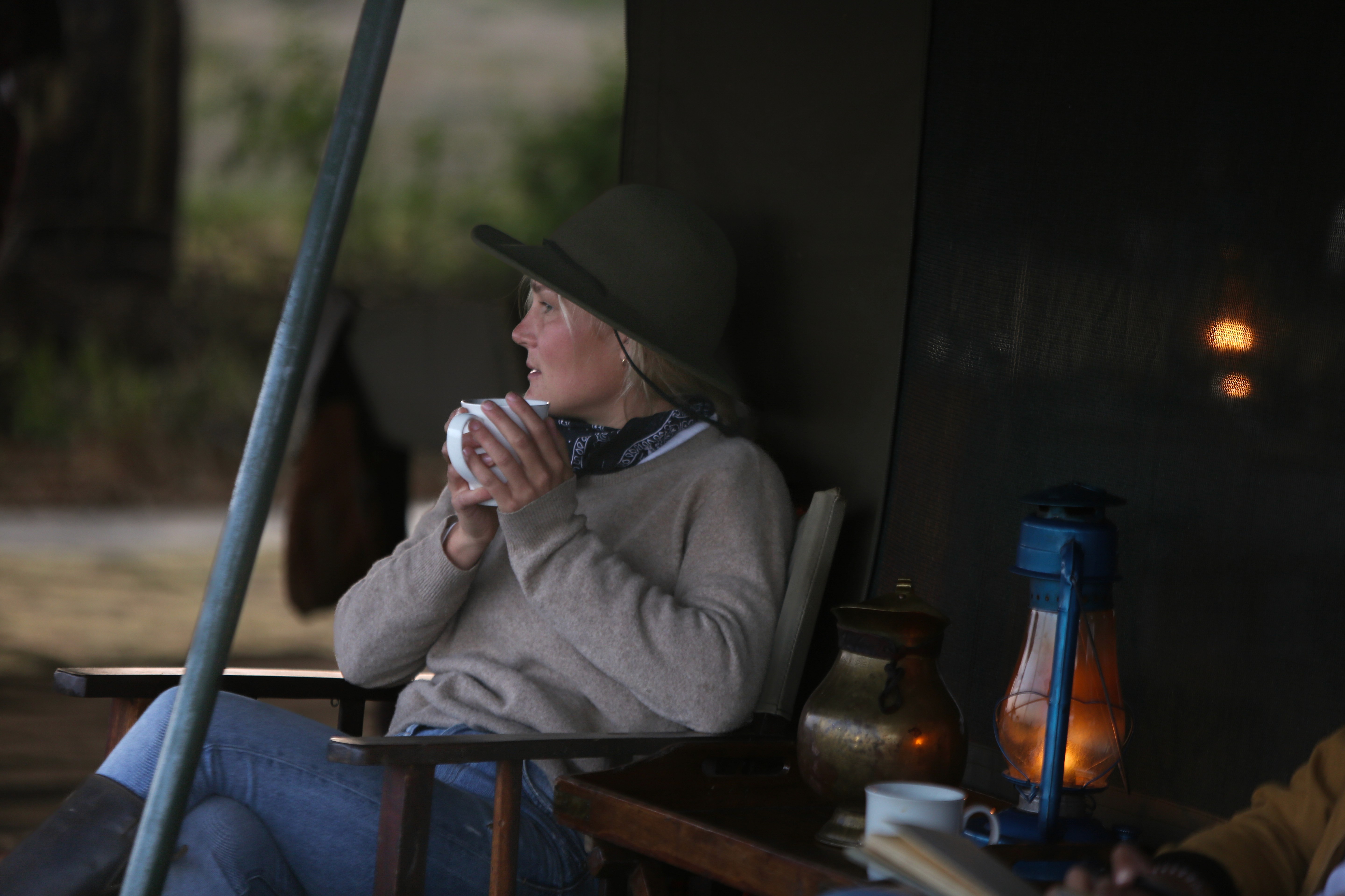 Kilimanjaro Elephant Ride, Arusha, Tanzania. En kvinna sitter och läser utanför ett tält uppsatt i vildmarken.