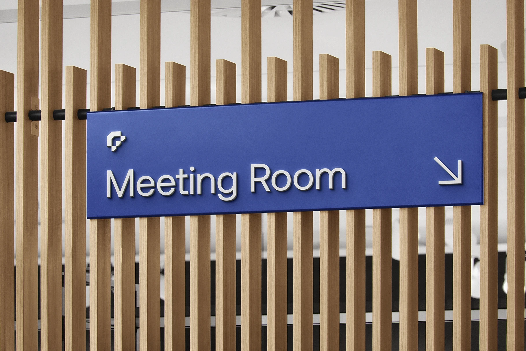 Office wayfinding sign mockup in blue for a meeting room on a wood slat wall.