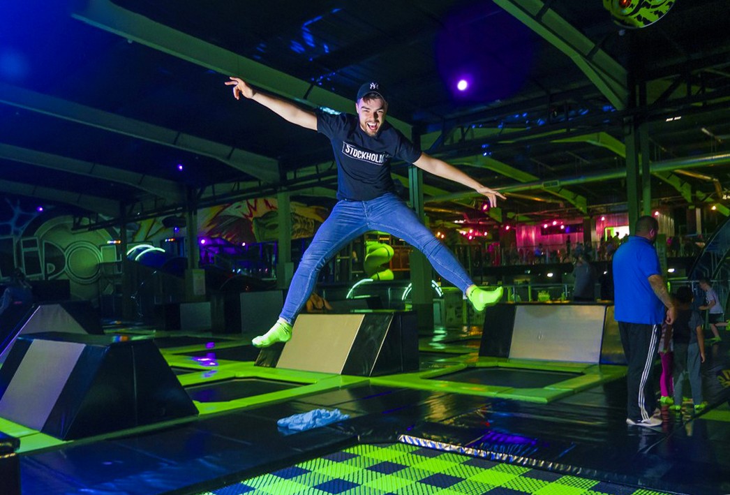 Young adult jumping mid-air on a trampoline, excited and happy at Flip Out Trampoline Park