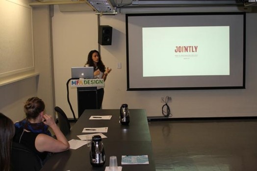A photo of a woman giving a lecture from a laptop while on the screen projector there is the word JOINTLY.