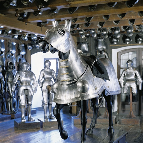 一个博物馆展厅陈列着中世纪盔甲，包括骑马的骑士和穿戴在模特上的各种盔甲。