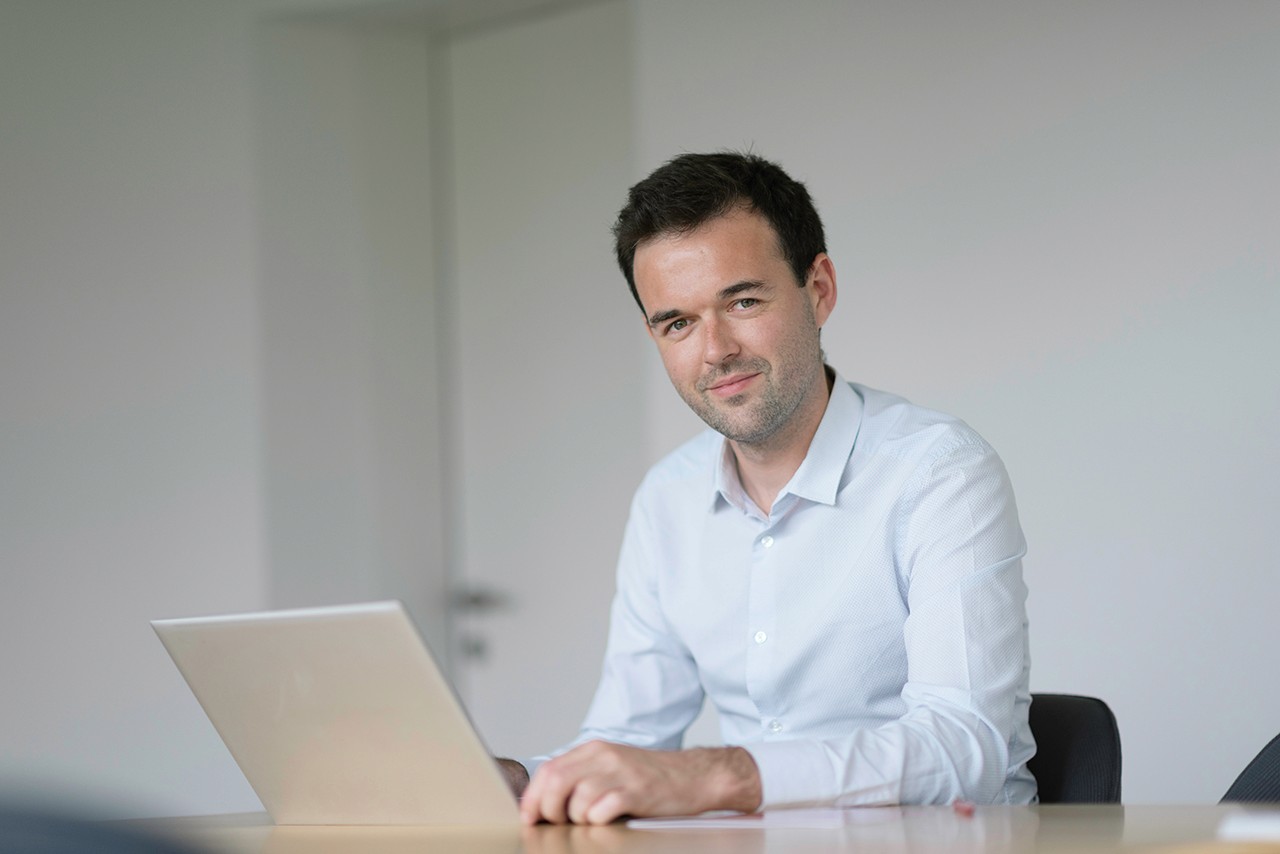 Professional portrait of a Team member, sitting at a table with a laptop and a confident expression.