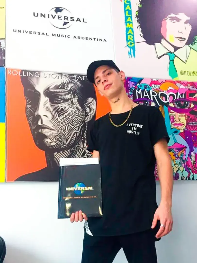 A young man stands in front of a wall featuring a collection of album covers, likely promoting Universal Music Argentina.