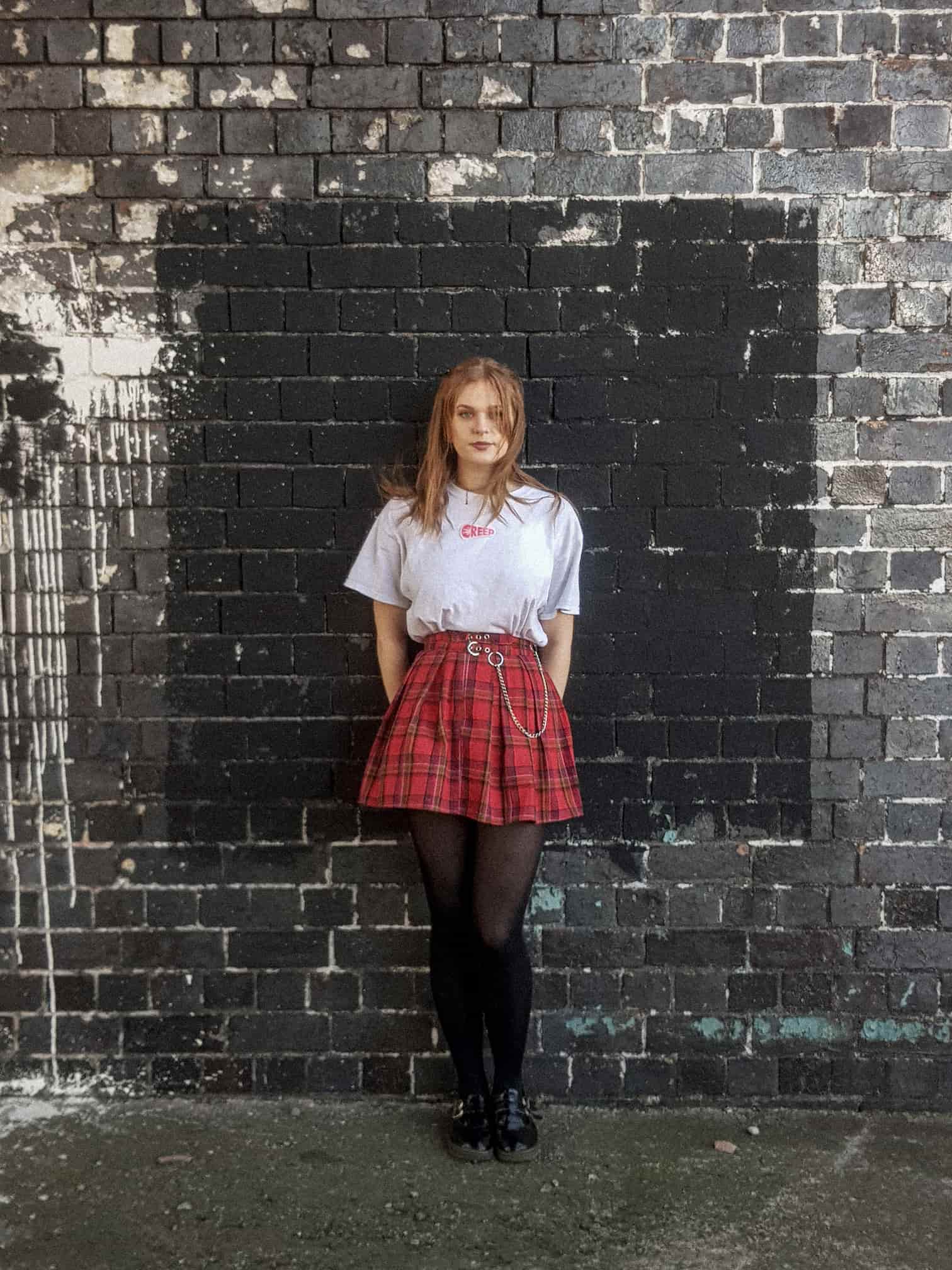 Photograph of streetwear model wearing creep branded clothing against dark brick wall.