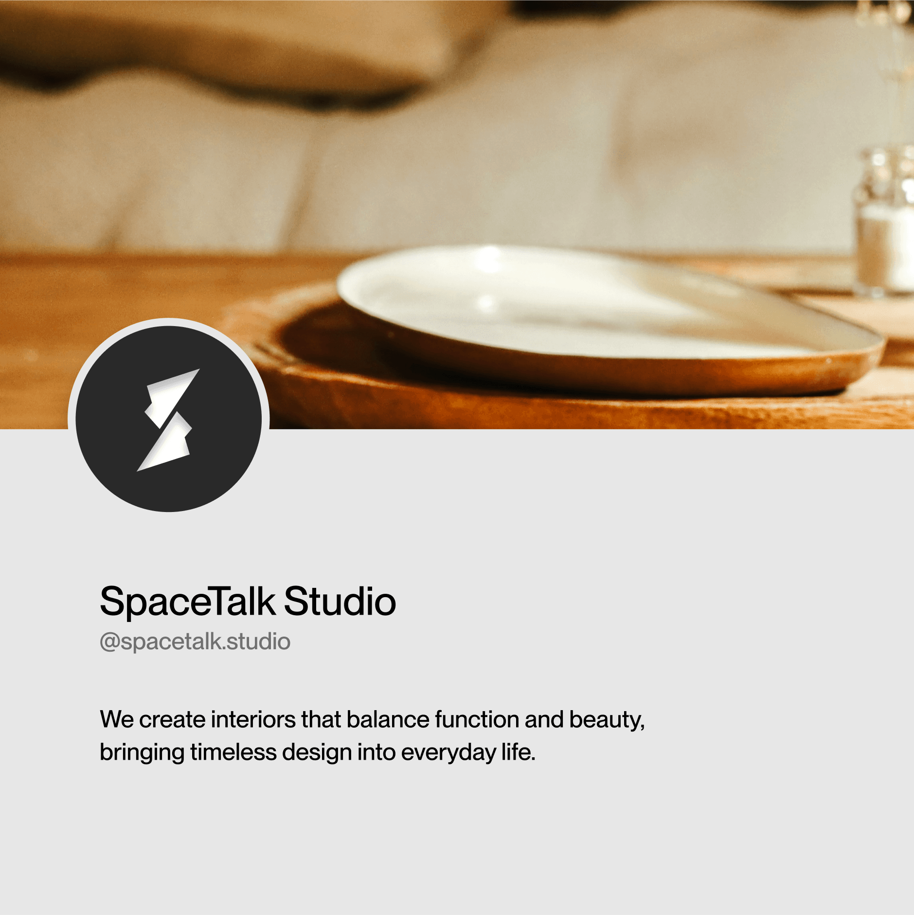 A round wooden table in a cozy, modern interior setting holds a small decorative vase, with text below stating "SpaceTalk Studio" and a description about creating interiors that blend form and beauty.