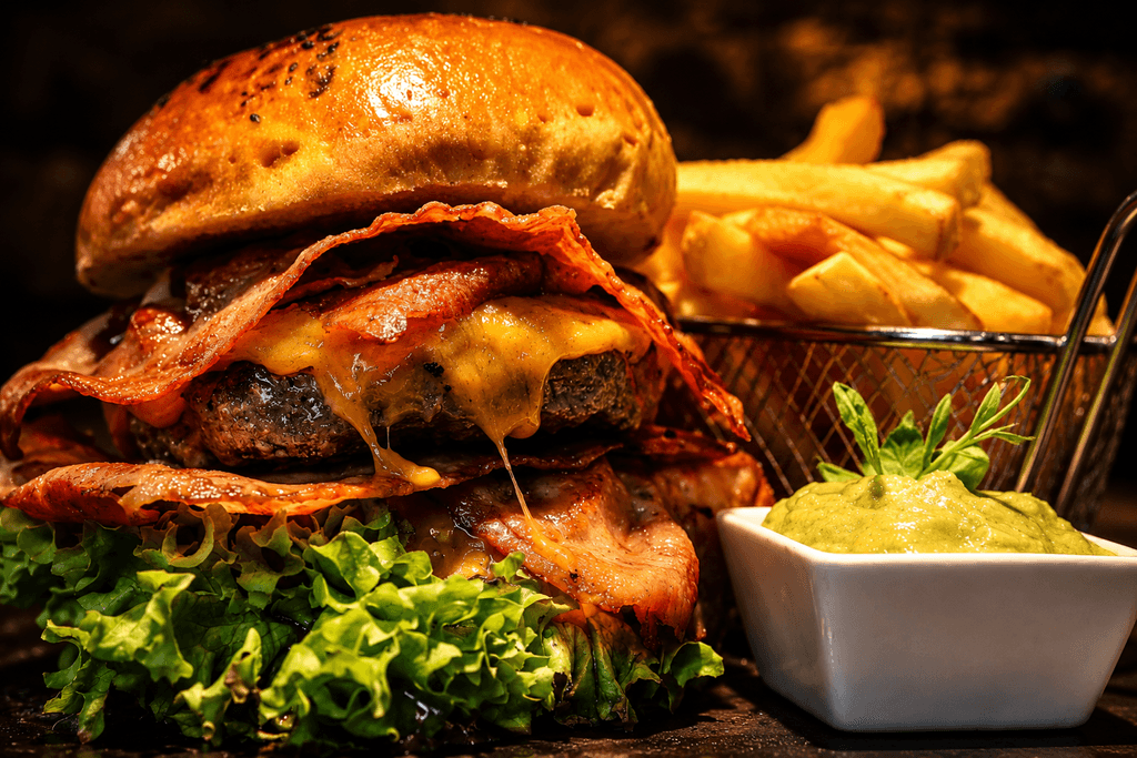 Overhead view of a kAlps Foodbar table spread with burgers, crispy fries, fondue dishes, a red cocktail, dipping sauces, and fresh garnishes arranged on slate serving boards.