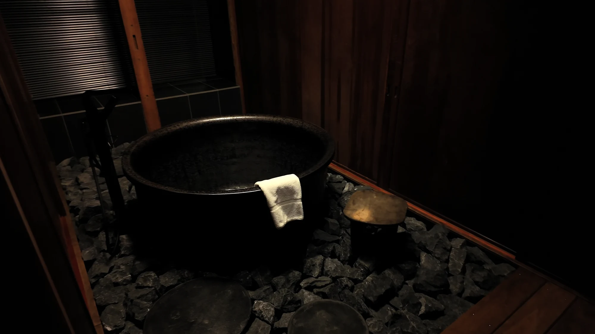 A dark iron soaking tub set into a timber floor in a Kinosaki guest room.
