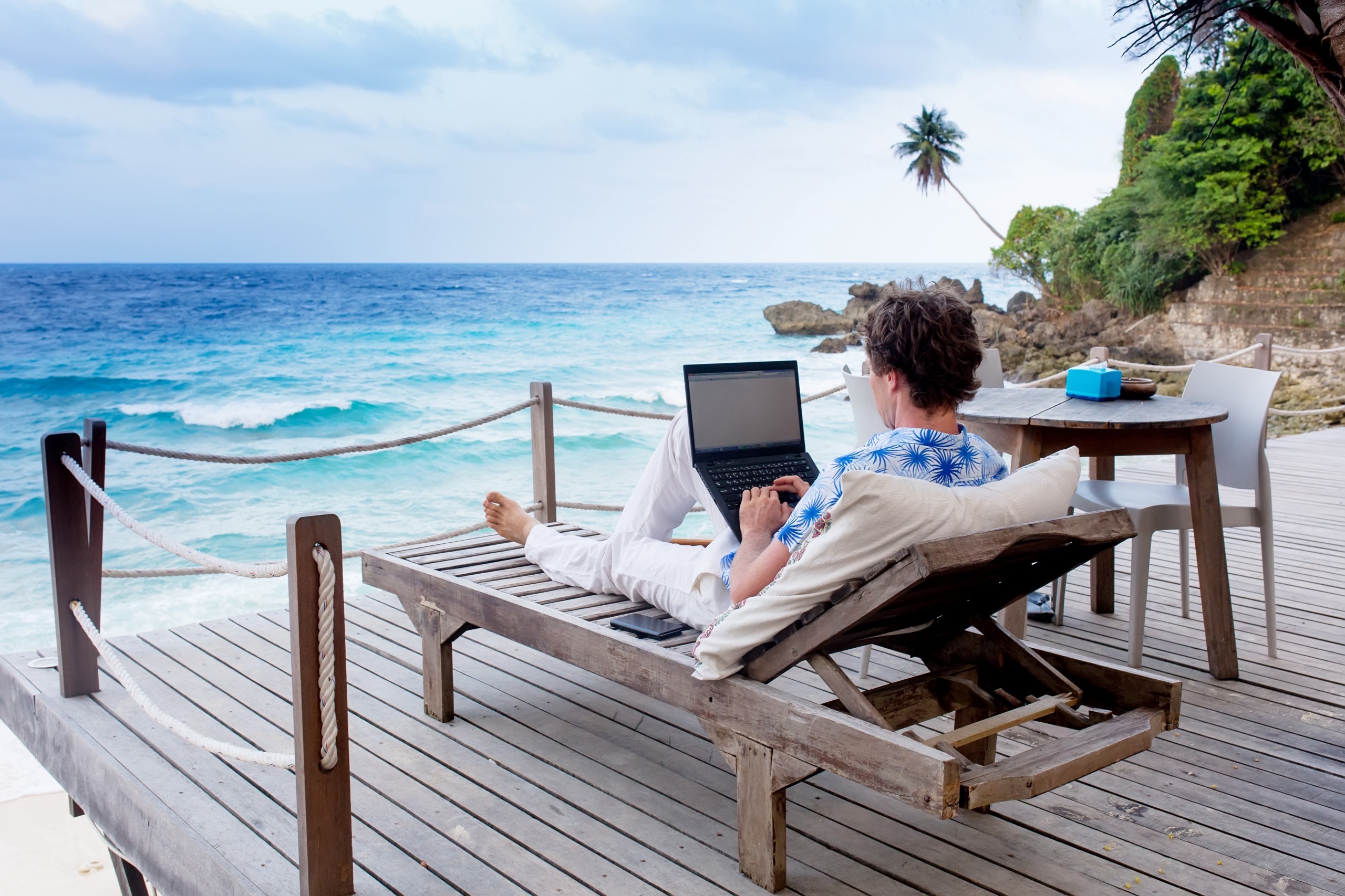 Homem trabalhando em frente a praia com notebook 