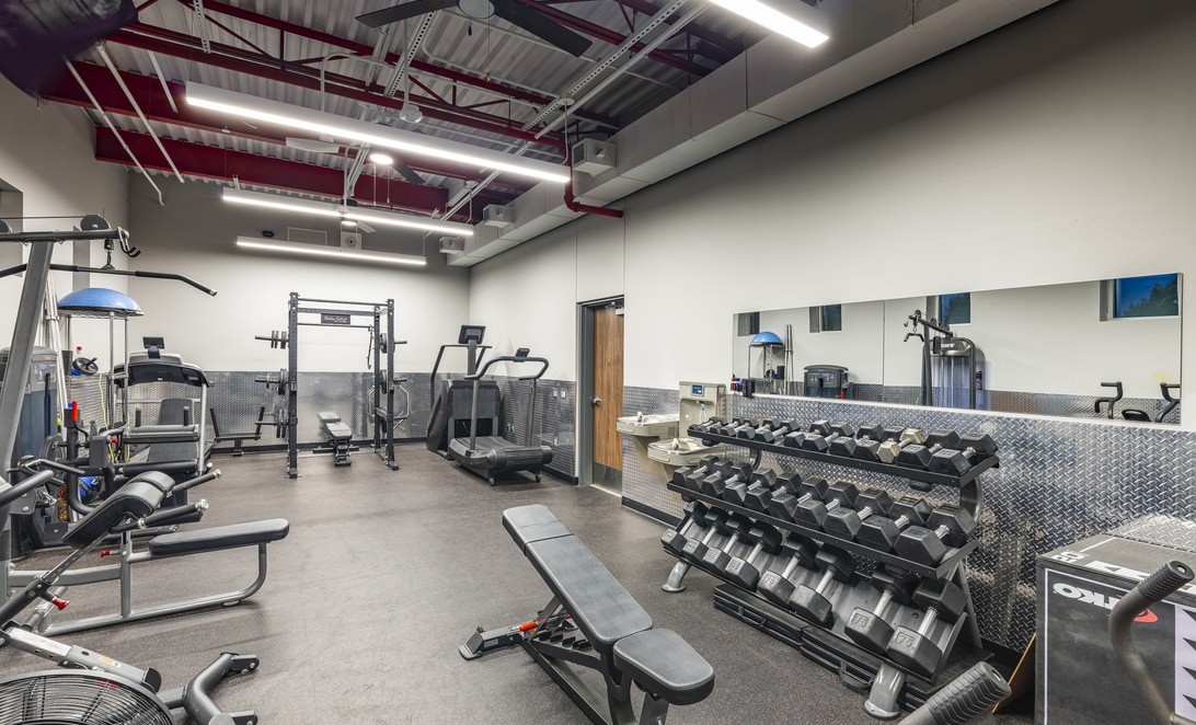 Fitness room with cable machine and dumbbell rack along mirrored wall at Plano Fire Station 5, by Martinez Architects.